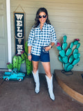 Woman in a checkered shirt and shorts standing in front of decorative cacti and a 'Welcome' sign.