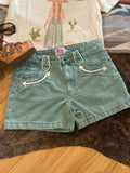 A pair of light turquoise denim shorts with white embroidered arrow details on the front pockets, laid flat on a brown fur rug with a wooden floor visible underneath.