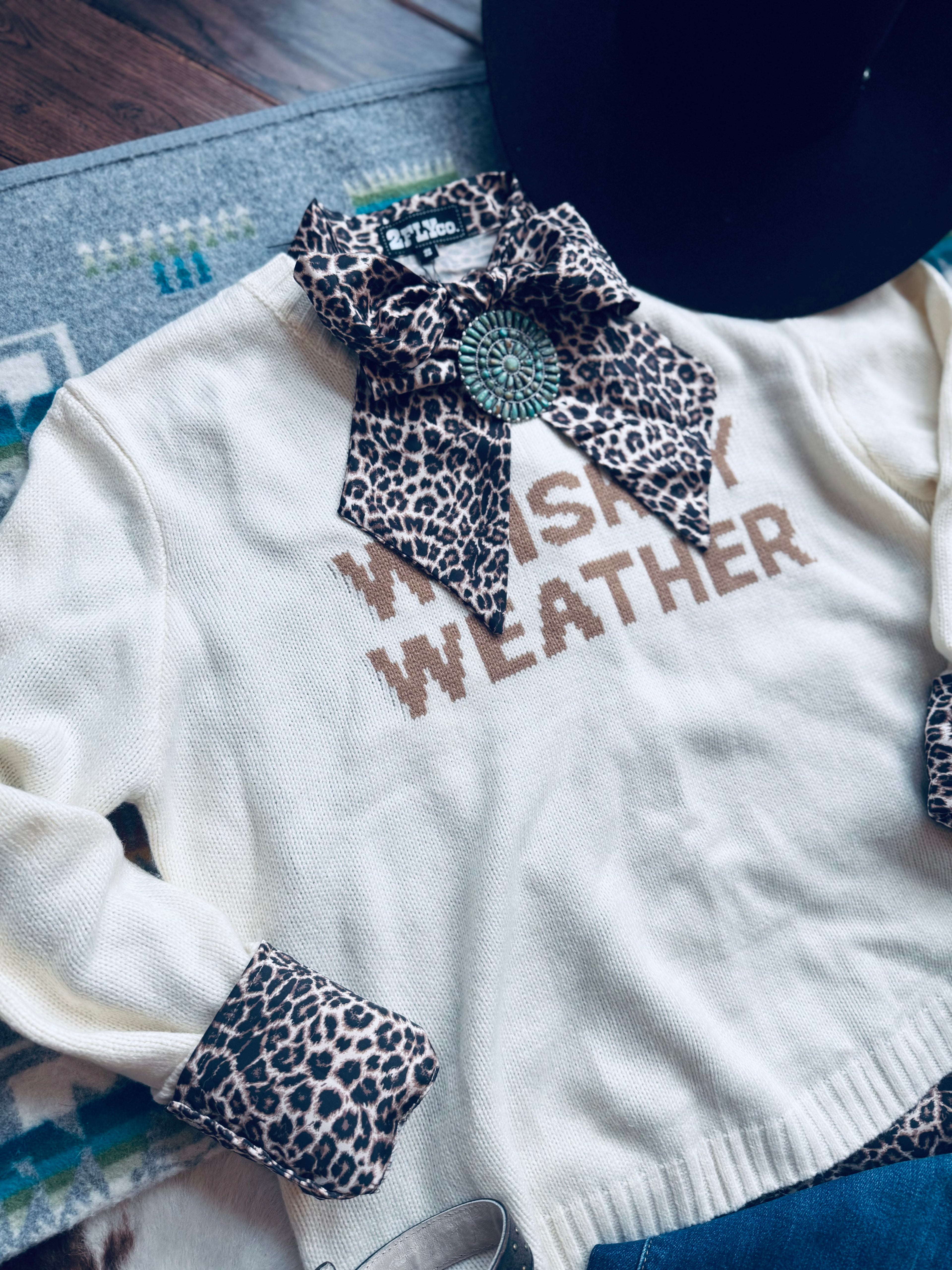 White sweater with leopard print accents and 'Whiskey Weather' text on a textured surface.