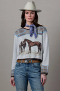 A model wearing a light gray knit sweater with a horse graphic, patterned houndstooth shoulder and cuff details, a blue neck scarf, blue jeans, and a white cowboy hat, posed against a neutral gray background.