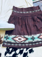 A dark brown A-line skirt/skort with a wide Southwestern geometric pattern border, styled flat-lay on a white surface with a white sneaker partially visible.