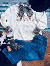 Load image into Gallery viewer, White sweater with &#39;Whiskey Weather&#39; text, blue jeans, leopard print accessories on a patterned surface.

