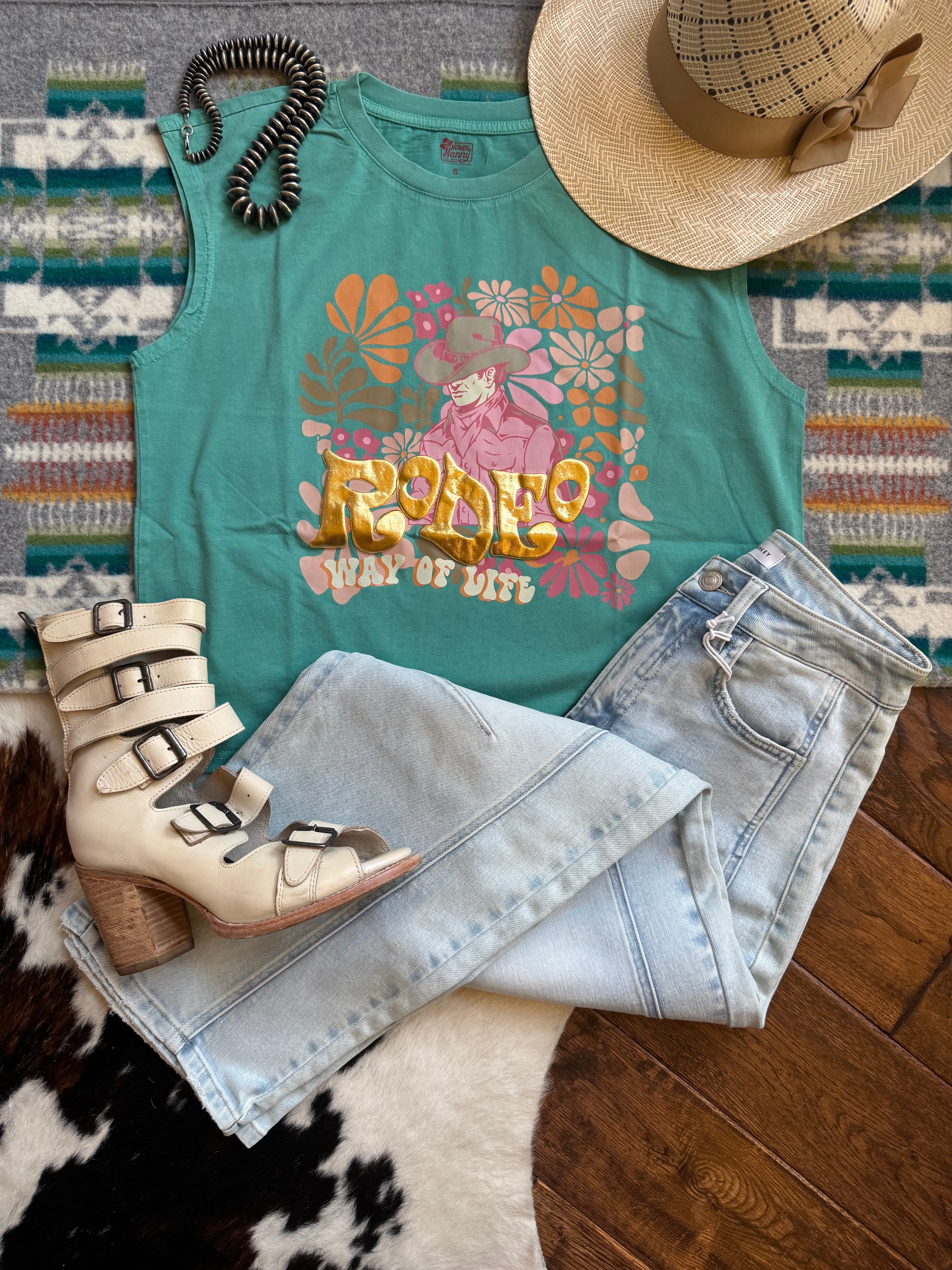 Teal t-shirt with floral design, jeans, beige boots, and a hat on a patterned rug.